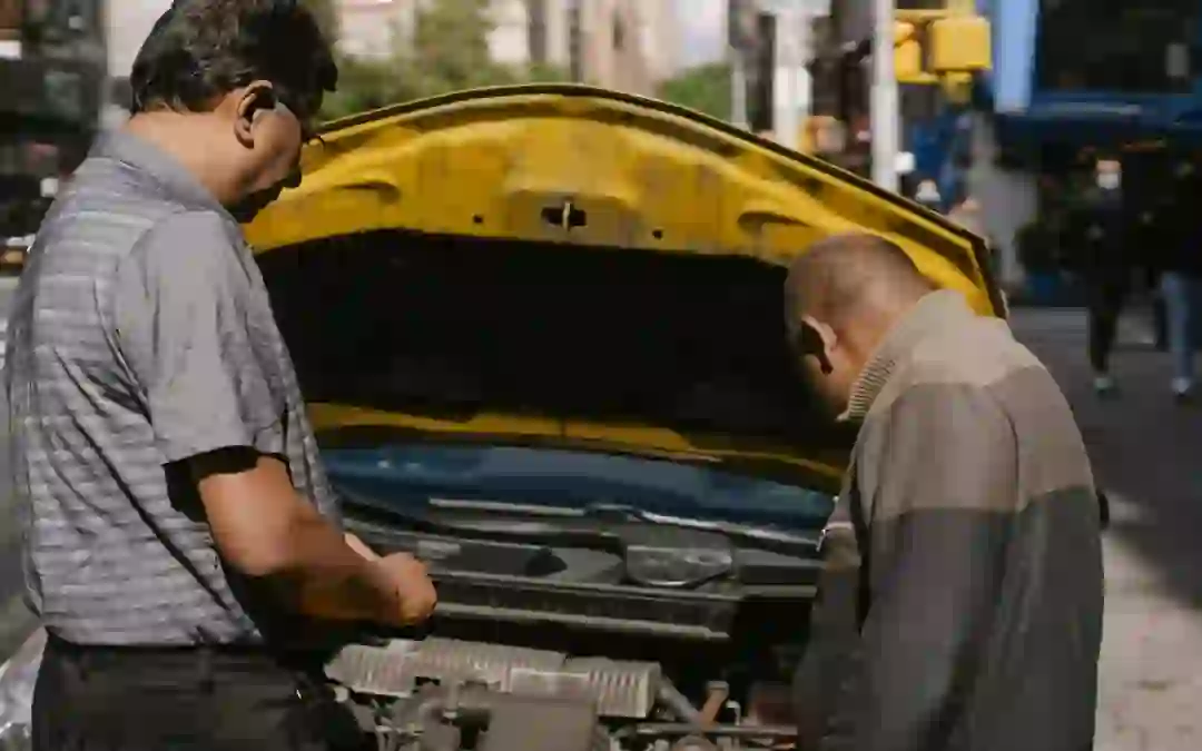 Two men inspecting engine under open hood of a yellow car, repair or scrap after failed safety inspection in Ontari