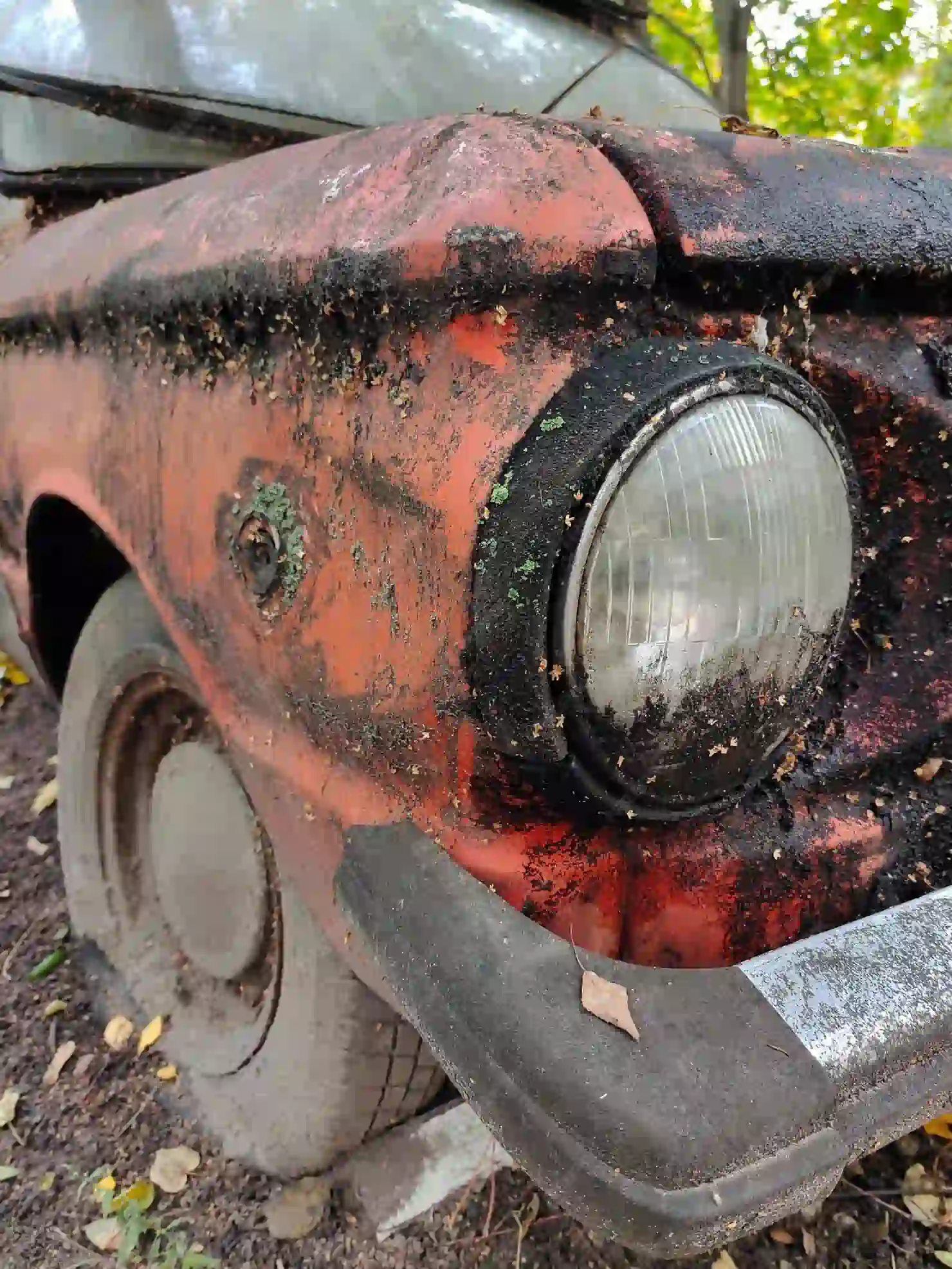 A heavily rusted junk car with peeling red paint, flat tires, and dirt buildup abandoned and ready for scrap removal.