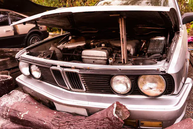 Non-running scrap car with open hood stripped of parts