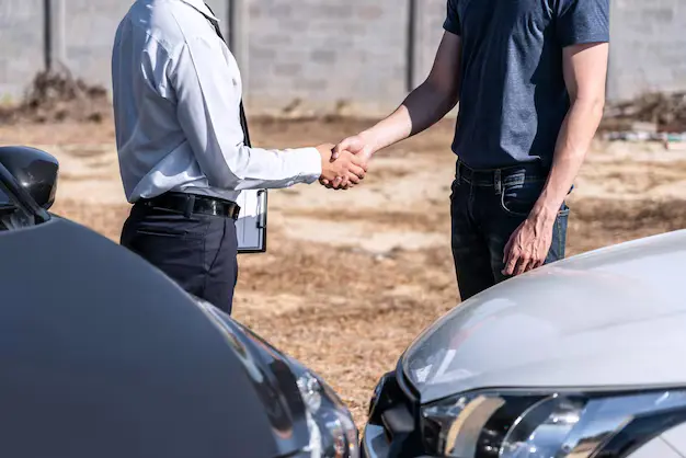 Two men shake hands beside cars, sealing a junk car sale deal outdoors.