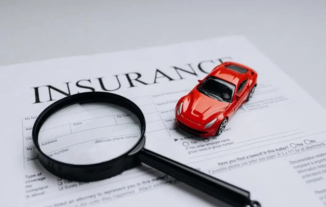 A red toy car and magnifying glass placed on a printed car insurance form