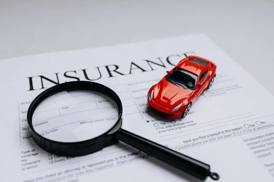 A red toy car and magnifying glass placed on a printed car insurance form