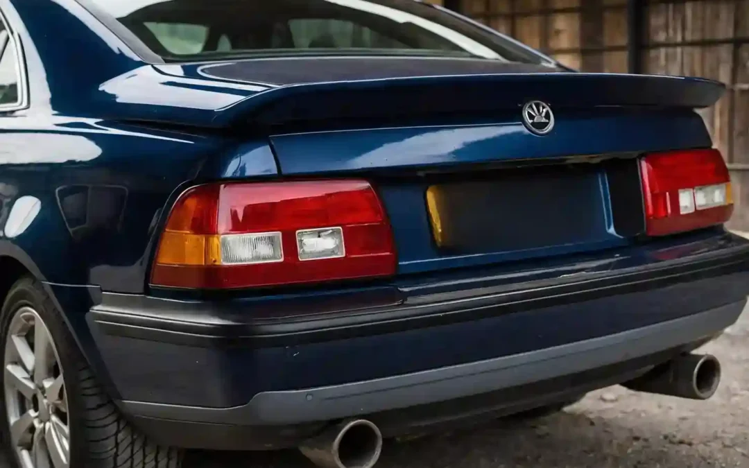 Rear view of a navy blue sedan with red tail lights, dual exhaust, rear spoiler, and blurred license plate