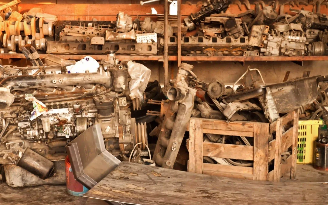 A salvage yard workshop filled with used engine blocks and scrap car parts stacked on rusty shelves.
