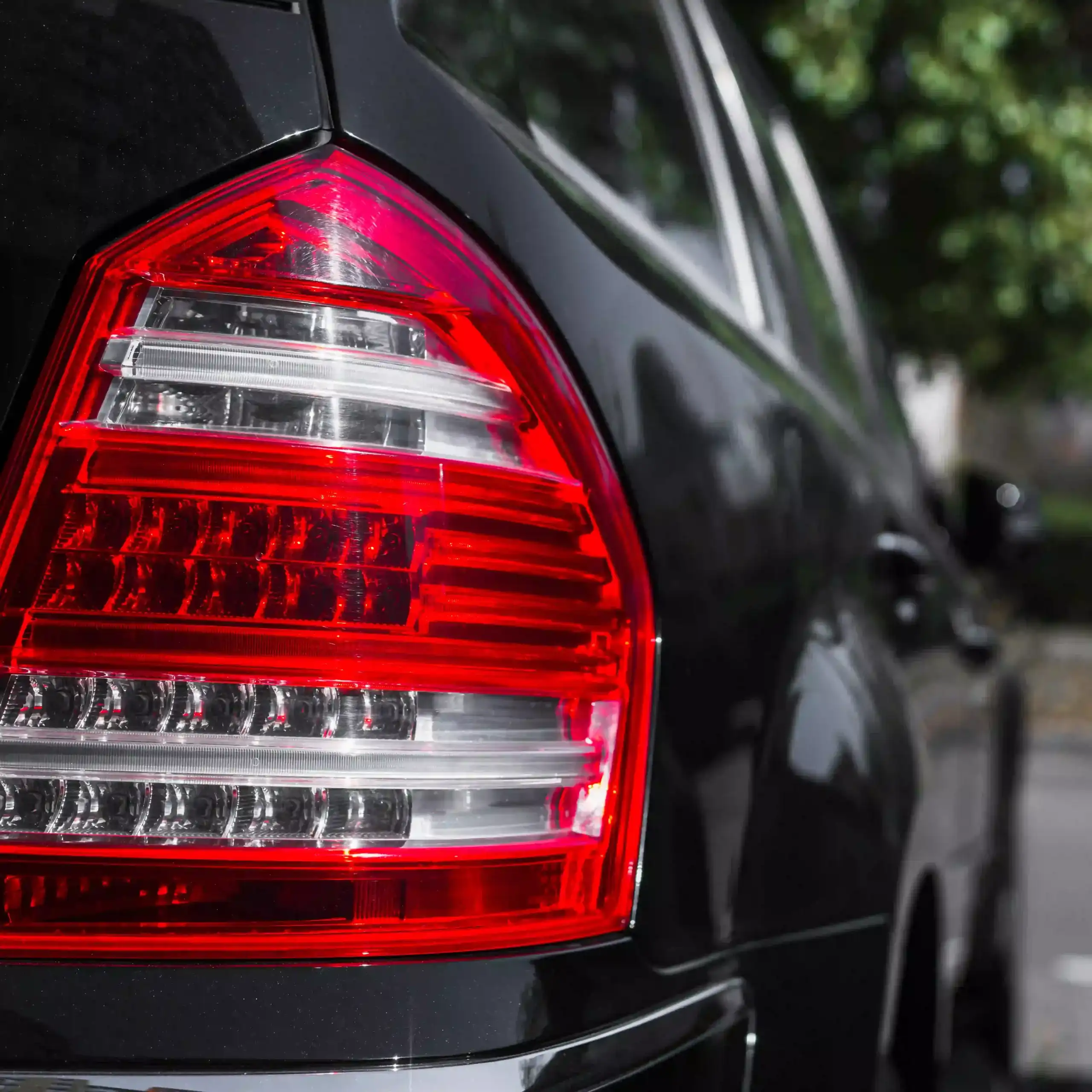 Make-Model-and-Year-scaled Close-up of a black car's rear taillight with red-and-clear LED design, highlighting sleek automotive styling and detail