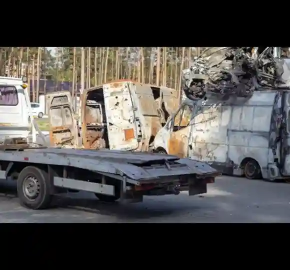 Flatbed tow truck loading burnt, wrecked vehicles at a scrap yard, showcasing junk car removal services.